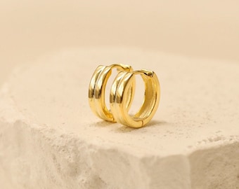 May include: A pair of gold hoop earrings with a thick, rounded design. The earrings are simple and elegant.