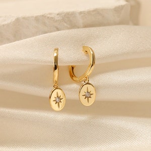 May include: A pair of gold hoop earrings with a dangling oval charm featuring a small, sparkling star in the centre.