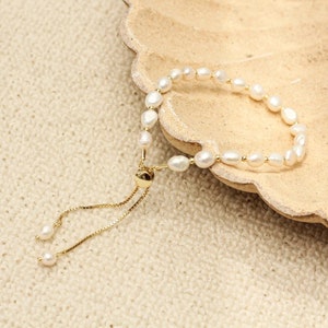 May include: A white pearl bracelet with a gold adjustable clasp. The bracelet is made of small, round pearls and has a delicate, feminine look.