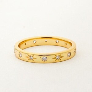 K&ouml;nnte beinhalten: Ein Goldring mit einer Reihe kleiner Diamanten, die in sternf&ouml;rmigen Designs gefasst sind.