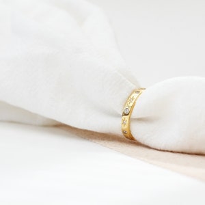 K&ouml;nnte beinhalten: Ein goldener Ring mit kleinen, klaren Steinen, die in einem Sternmuster um das Band herum gesetzt sind.