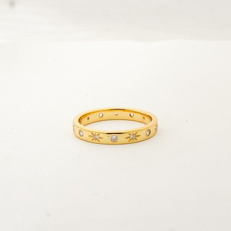 K&ouml;nnte beinhalten: Ein Goldring mit einer Reihe kleiner Diamanten, die in sternf&ouml;rmigen Designs gefasst sind.