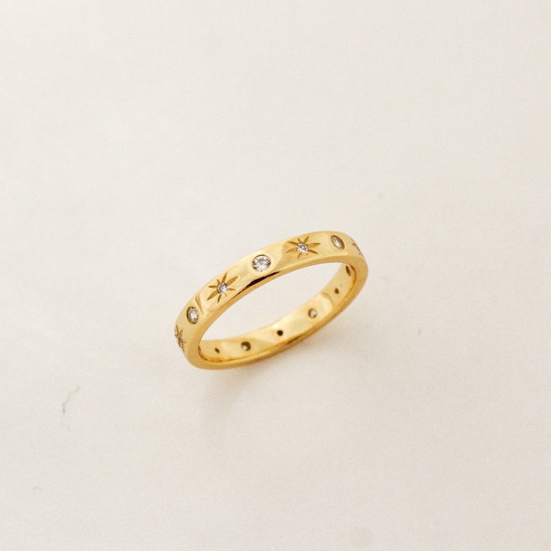 K&ouml;nnte beinhalten: Ein Goldring mit einem sich wiederholenden Muster aus kleinen Sternen und Diamanten.