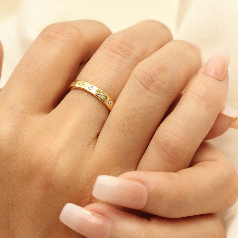 K&ouml;nnte beinhalten: Ein goldener Ring mit kleinen, klaren Steinen, die in einem Sternmuster eingefasst sind.