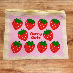 Op de afbeelding: Een canvas etui met een roze rechthoekig ontwerp met rode aardbeien met groene bladeren en de tekst "Berry Cute". De etui heeft een gele rits en een natuurlijke canvas rand.