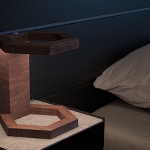 Puede incluir: Una lámpara de mesa de noche de madera con una base hexagonal y una pantalla hexagonal. La lámpara está hecha de madera oscura y tiene un brillo cálido y acogedor.