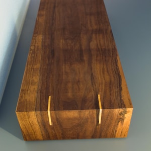May include: A rectangular wooden box with a rich, dark brown finish. The box features vertical gold-colored inlays on the sides. The wood grain is visible, adding to the natural aesthetic. The box is likely for storage or display.