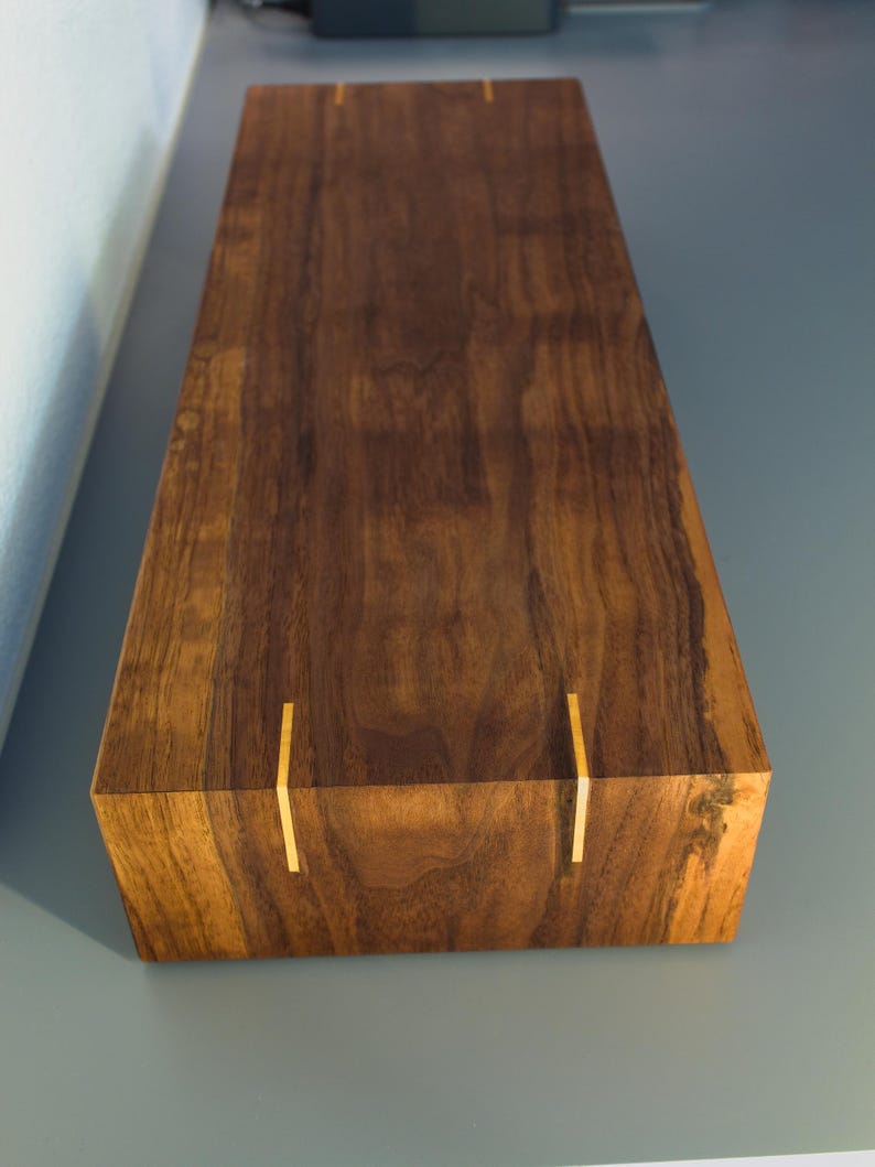May include: A rectangular wooden box with a rich, dark brown finish. The box features vertical gold-colored inlays on the sides. The wood grain is visible, adding to the natural aesthetic. The box is likely for storage or display.