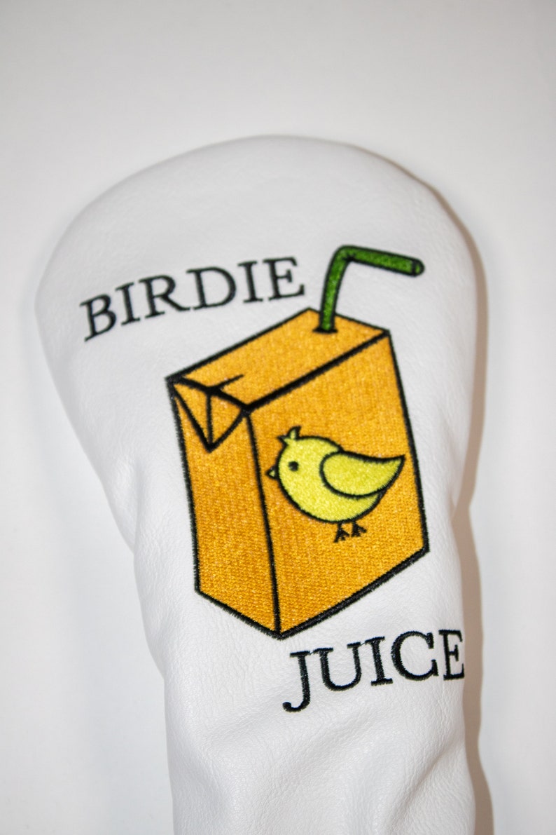 May include: White golf headcover with an embroidered image of a yellow juice carton with a green straw and a yellow bird. The text "BIRDIE JUICE" is embroidered on the headcover.