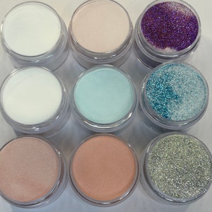 May include: Nine small jars of nail polish, including white, light pink, light blue, and three different shades of glitter.