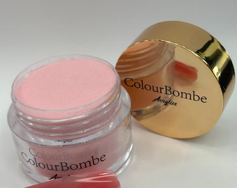 Puede incluir: Un polvo acrílico rosa en un frasco transparente con tapa dorada. El frasco tiene el texto "ColourBombe Acrylics" en la tapa. Se muestra una punta de uña rosa en primer plano.