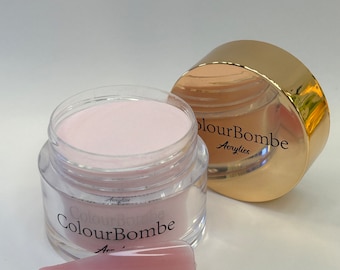 Puede incluir: Un frasco transparente con polvo acrílico rosa en su interior. El frasco tiene una tapa dorada con el texto "ColourBombe Acrylics". Una punta de uña de acrílico rosa está en primer plano.