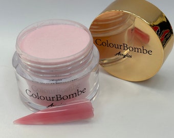Puede incluir: Un polvo acrílico rosa en un frasco transparente con tapa dorada. El frasco está etiquetado con "ColourBombe Acrylics". Se muestra una punta de uña acrílica rosa junto al frasco.