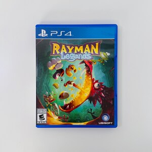 Może przedstawiać: Niebieskie pudełko na grę PlayStation 4 Rayman Legends. Okładka przedstawia wielką czerwoną istotę z otwartą paszczą, postać Raymana oraz różne unoszące się obiekty. Widoczne jest logo Ubisoft oraz oznaczenie wieku PEGI 7 na froncie opakowania.