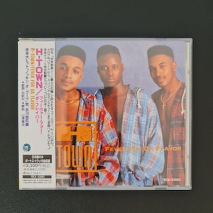 以下が含まれることがあります： H-TOWNのアルバム「Fever For Da Flavor」のCDケース。青い背景の前に3人の男性がいます。CDケースには、アルバムタイトルを含む英語と日本語のテキストが含まれています。