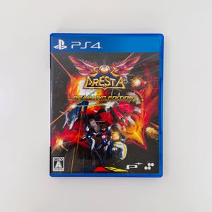 以下が含まれることがあります： PlayStation 4用ゲームソフト「ソルクレスタ ドラマティックエディション」の青いパッケージ。カバーアートには、赤、オレンジ、黄色の爆発が描かれた鮮やかな宇宙戦のシーン、中央の金色のロゴ、そして手前に3人のキャラクターが配置されています。