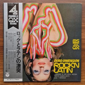 May include: A vintage vinyl record album cover featuring a woman with colorful body paint in red, green, and white. The album title is "Quad Dimension Rock'n Latin" with Japanese text and the artist's name. The record is a 4-channel QX record.