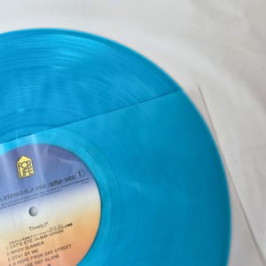 May include: A vibrant, turquoise vinyl record with the text "Timely!!" and a tracklist visible. The record is partially encased in a clear plastic sleeve. The label features the "FOR LIFE" logo and Japanese text.