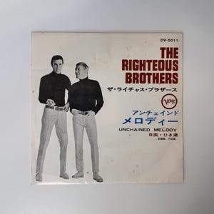 May include: A square vinyl record sleeve featuring a black and white photograph of two individuals in black long-sleeved shirts and light-colored trousers. The text reads THE RIGHTEOUS BROTHERS, UNCHAINED MELODY, EBB TIDE, and Japanese characters.