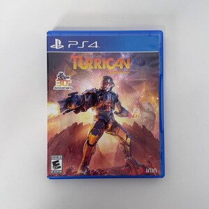 以下が含まれることがあります： PlayStation 4用ゲームソフト「Turrican Flashback」の青いプラスチックケース。カバーアートには、燃えるような岩場の風景を背景に、武器を構えた未来的な装甲キャラクターが描かれている。テキストにはPS4、Turrican Flashback、30th Anniversary、ESRB E10+が含まれている。