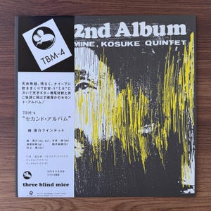 May include: A vinyl record cover featuring a dark gray background with abstract yellow vertical lines and a white obi strip on the left side. The text reads 2nd Album, Mine, Kosuke Quintet, TBM-4, and three blind mice, along with Japanese text.