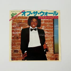 Può includere: Una copertina di un album vintage con Michael Jackson in smoking nero con papillon, sullo sfondo di un muro di mattoni. Il titolo dell'album "Off The Wall" è visualizzato in inglese e giapponese, con il nome dell'artista in evidenza.