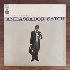 May include: A square vinyl record cover featuring a black and white photograph of a smiling person in a suit holding a trumpet and a briefcase. The text reads European Concert Recordings by AMBASSADOR SATCH, with CBS SONY logos in the corner.