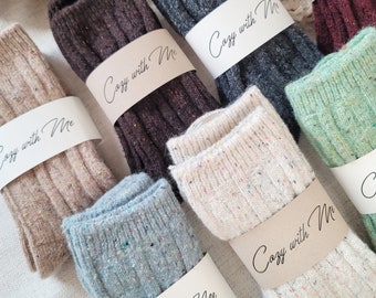 May include: A collection of six pairs of cozy socks with speckled patterns. Each pair has a brown paper tag with the text "Cozy with Me" written in black.