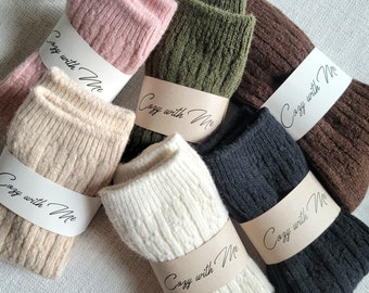 May include: Six pairs of knitted socks in various colors, including pink, beige, white, green, brown, and black. Each pair has a brown paper tag with the text "Cozy with Me" written in black.