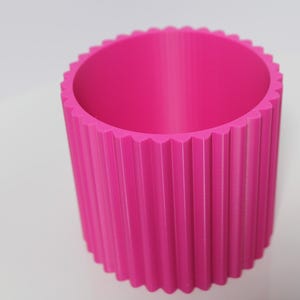May include: A bright pink cylindrical planter with a fluted design. The planter is made of a smooth, plastic material.