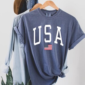 May include: A navy blue t-shirt with the word "USA" printed in white with a small American flag underneath.