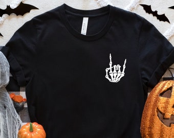 May include: Black t-shirt with a white skeleton hand making the rock and roll hand gesture. The shirt is surrounded by Halloween decorations, including pumpkins, bats, and spiders.