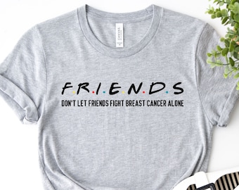 May include: Gray t-shirt with the text "FRIENDS" in black with colorful dots between the letters. Below the text is the phrase "Don't let friends fight breast cancer alone."