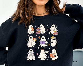 Puede incluir: Una sudadera negra con un gráfico de varios fantasmas sosteniendo libros. Los fantasmas están en varias poses, algunos están leyendo, otros están sosteniendo pilas de libros. El gráfico está en un estilo de dibujos animados con colores brillantes.