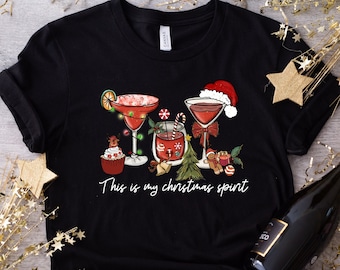 May include: Black t-shirt with a Christmas-themed design featuring three cocktails, a cupcake, and a small Christmas tree. The text "This is my Christmas spirit" is printed below the design.