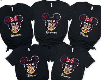 May include: Five black t-shirts with a Mickey Mouse head design. The design features a red and white polka dot bow, fireworks, and Disney characters. Each shirt has a different family member's name: Grandma, Brother, Sister, Daddy, and Mommy.