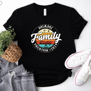 May include: Black t-shirt with a vintage-style graphic that says "Miami Family Vacation 2026" with a palm tree and sun graphic. The text "Daddy" is in a smaller font and is located below the main text.