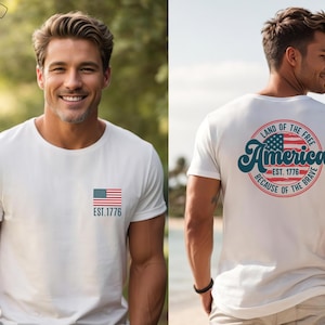 May include: A gray t-shirt with a small American flag on the front and a larger circle design on the back. The circle design features a larger American flag, the text "Land of the Free", "America", "Est. 1776", and "Because of the Brave".