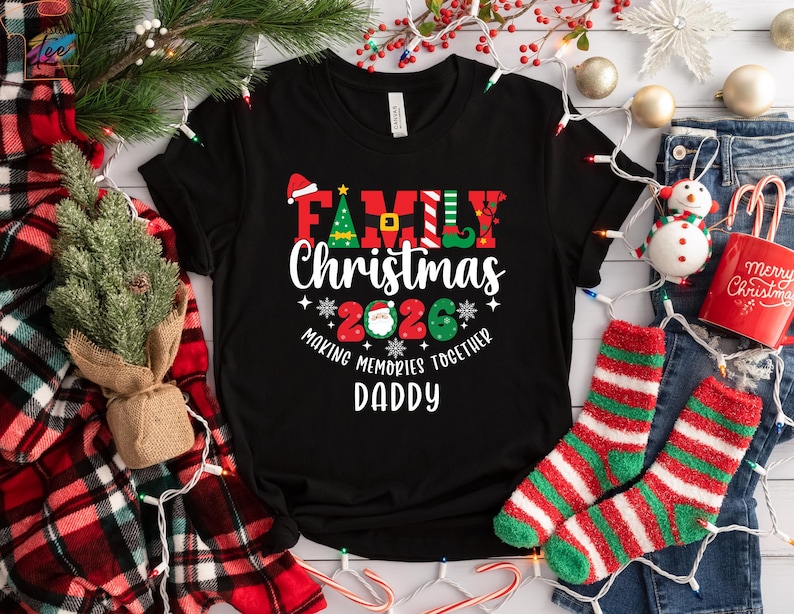 May include: Black t-shirt with the text "Family Christmas 2026 Making Memories Together Daddy" in red, green, and white. The shirt has a Christmas tree and Santa hat graphic. The shirt is displayed with Christmas decorations.