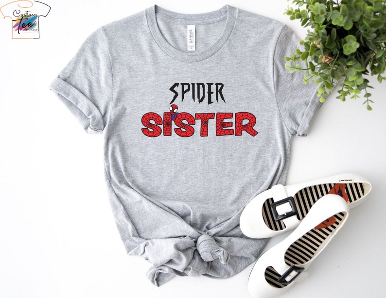 Puede incluir: Camiseta gris con el texto "SPIDER SISTER" en negro con un gr&aacute;fico rojo de Spider-Man en la "S" de hermana.