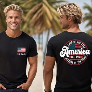May include: A gray t-shirt with a small American flag on the front and a larger circle design on the back. The circle design features a larger American flag, the text "Land of the Free", "America", "Est. 1776", and "Because of the Brave".