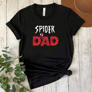 Puede incluir: Camiseta negra con un gr&aacute;fico blanco que dice "Spider Dad" con una imagen de dibujos animados de Spiderman en el medio de la palabra "Dad".