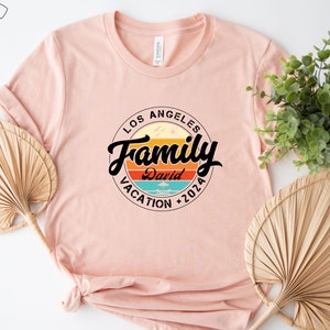 May include: A pink t-shirt with a circular design featuring the text "Los Angeles Family Vacation 2026" with a retro sunset graphic and the name "David" in the center.