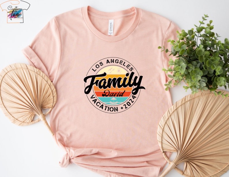 May include: A pink t-shirt with a circular design featuring the text "Los Angeles Family Vacation 2026" with a retro sunset graphic and the name "David" in the center.