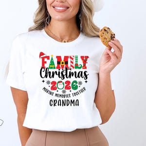 May include: White t-shirt featuring a Christmas graphic. The design includes the words "FAMILY Christmas 2026" in red, green, and black, with festive elements like a Santa hat, Christmas tree, and elf shoes. The text "Making Memories Together Grandma" is also included.