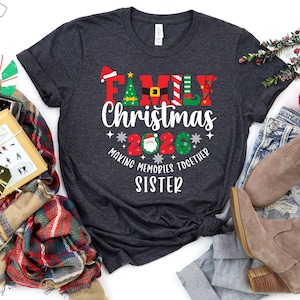 May include: A dark grey t-shirt featuring the text "FAMILY Christmas 2020" in festive colours. The design includes a Santa hat, Christmas tree, and elf details. The words "MAKING MEMORIES TOGETHER SISTER" are also printed on the shirt, perfect for the holiday season.