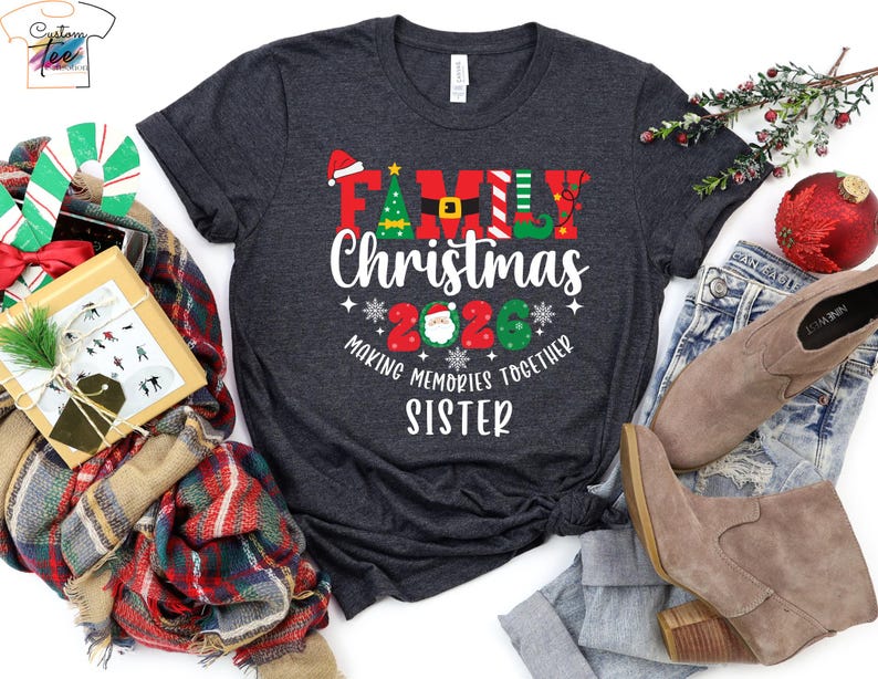 May include: A dark grey t-shirt featuring the text "FAMILY Christmas 2020" in festive colours. The design includes a Santa hat, Christmas tree, and elf details. The words "MAKING MEMORIES TOGETHER SISTER" are also printed on the shirt, perfect for the holiday season.