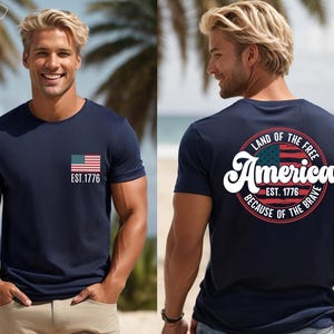 May include: A gray t-shirt with a small American flag on the front and a larger circle design on the back. The circle design features a larger American flag, the text "Land of the Free", "America", "Est. 1776", and "Because of the Brave".