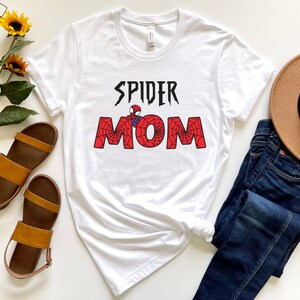 Puede incluir: Camiseta blanca con un gr&aacute;fico rojo y negro que dice "Spider Mom" con un dise&ntilde;o de telara&ntilde;a y una peque&ntilde;a imagen de Spiderman.