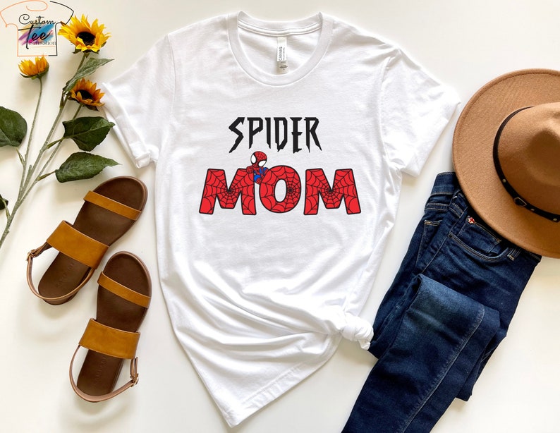 Puede incluir: Camiseta blanca con un gr&aacute;fico rojo y negro que dice "Spider Mom" con un dise&ntilde;o de telara&ntilde;a y una peque&ntilde;a imagen de Spiderman.